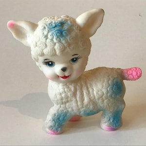 May include: A white rubber lamb toy with blue and pink accents. The lamb has a curly white fur texture and a sweet, smiling face with blue eyes.