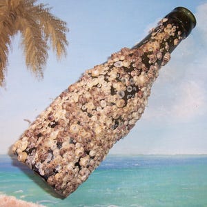 May include: A dark green glass bottle encrusted with small, beige and brown barnacles. The bottle is angled, showcasing the textured surface of the barnacles. The background features a painted beach scene with a palm tree and ocean.