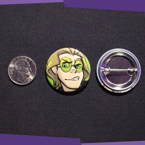 May include: A round button with a cartoon illustration of a person with green hair wearing green sunglasses. The person is smiling and looking to the side. The button is 1 inch in diameter and has a silver pin back.