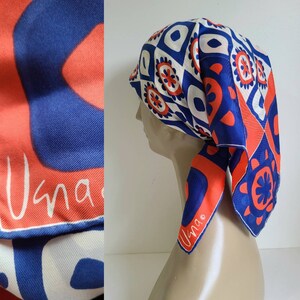 May include: A silk scarf with a geometric pattern in blue, white, and orange. The scarf is draped over a mannequin head. The word "Usna" is printed in white on an orange background.