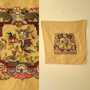 May include: A vintage needlepoint tapestry featuring a detailed design with a bird, deer, and floral elements in shades of red, blue, green, and brown. The tapestry is on a beige canvas, showcasing intricate stitching and a decorative border.