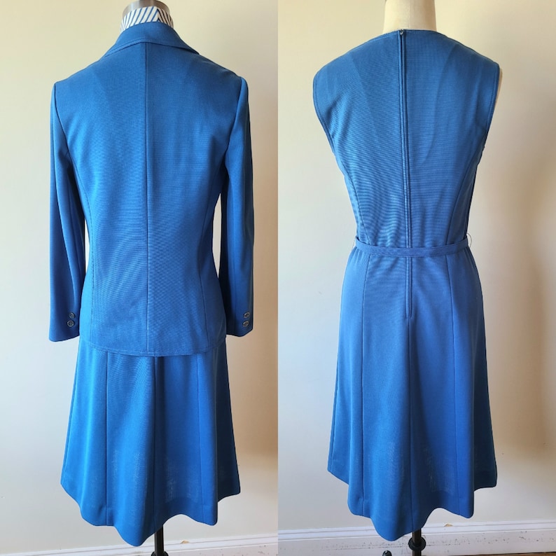 May include: A vintage blue skirt suit and a matching sleeveless dress. The suit includes a blazer with long sleeves and a knee-length skirt. The dress has a matching belt and a zipper down the back. The suit and dress are displayed on mannequins.