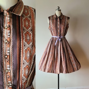 Puede incluir: Un vestido sin mangas con estampado geométrico marrón y naranja. El vestido tiene cuello y un lazo de cinta en la cintura.