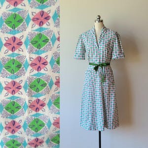 May include: A white dress with a green and pink geometric pattern. The dress has a collared neckline, short sleeves, and a green sash.