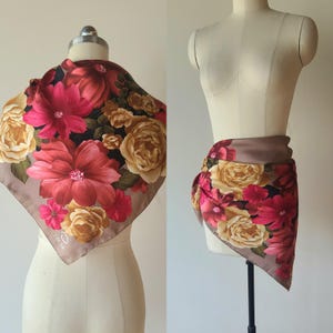 May include: A square scarf featuring a floral print with large red and cream-colored flowers on a black and taupe background. The scarf displays the word Oscar in the corner and is shown draped on a mannequin in two different styling positions.