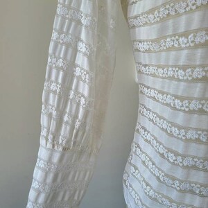 May include: White lace blouse with long sleeves and a striped pattern. The sleeves have a gathered detail at the cuffs.