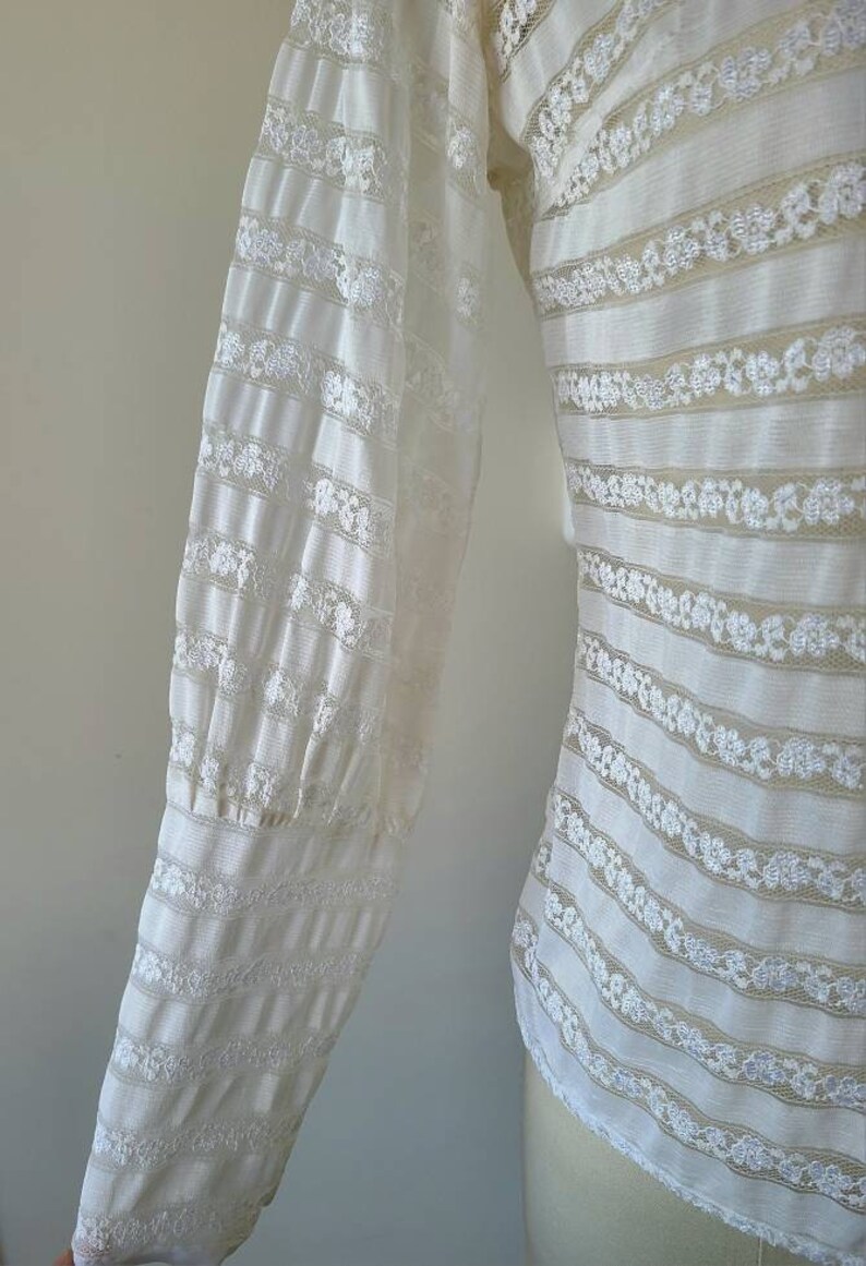 May include: White lace blouse with long sleeves and a striped pattern. The sleeves have a gathered detail at the cuffs.