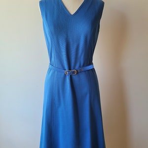 May include: A sleeveless, knee-length blue dress with a V-neck and a matching belt. The dress features vertical seams and a gold-colored buckle on the belt. The dress is displayed on a mannequin.