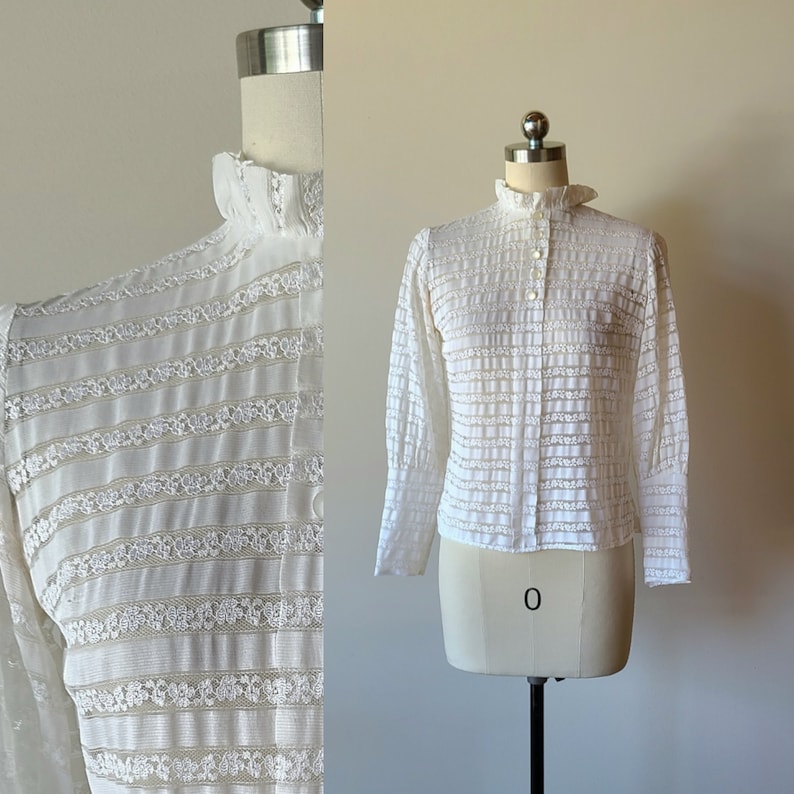 May include: White lace blouse with a high collar and long sleeves. The blouse has a button-up front and a delicate floral pattern.