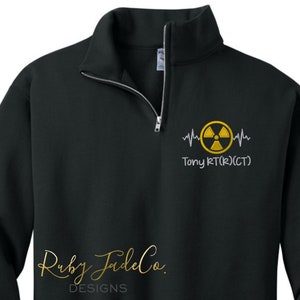 May include: Black 1/4 zip sweatshirt with a yellow radiation symbol and a heartbeat graphic. The text "Tony RT(R)(CT)" is embroidered below the graphic.