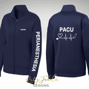 May include: Navy blue zip-up jacket with white text on the front and back. The front reads "name" and the back reads "PACU" with a heart and EKG line. The left sleeve reads "PERIANESTHESIA".
