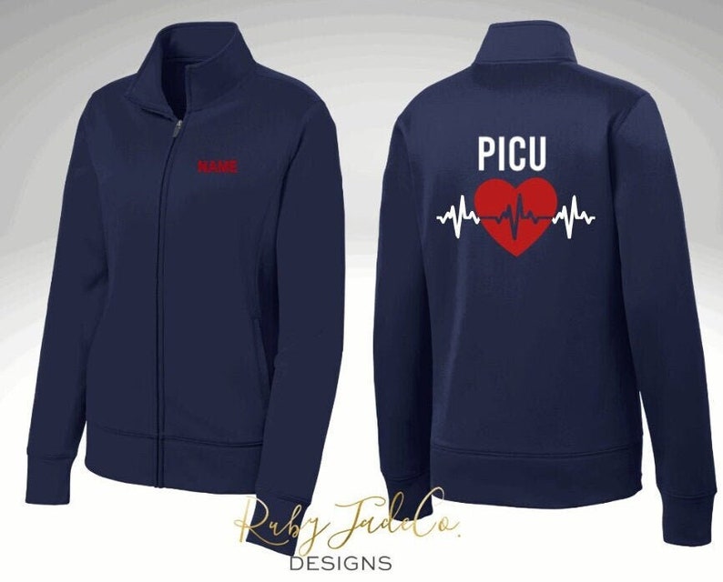 K&ouml;nnte beinhalten: Marineblaue Rei&szlig;verschlussjacke mit einem roten Herzen und einer EKG-Linie auf der R&uuml;ckseite. Der Text "PICU" befindet sich &uuml;ber dem Herzen. Die Vorderseite der Jacke hat den Text "NAME" auf der linken Brust gestickt.
