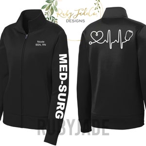 May include: Black fleece zip-up jacket with white text on the sleeve that reads "MED-SURG". The back of the jacket has a white heart with a stethoscope and heartbeat graphic. The front of the jacket has white text that reads "Nicole BSN, RN".
