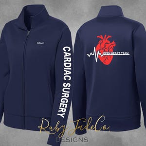 May include: Navy blue zippered jacket with a white "CARDIAC SURGERY" text on the left sleeve and a red heart with a heartbeat line and "OPEN HEART TEAM" text on the back.