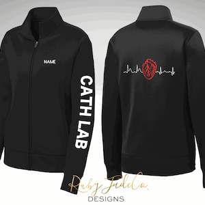 May include: Black zippered jacket with white text on the sleeve that reads "Cath Lab" and white text on the front that reads "Name". The back of the jacket has a red heart with a heartbeat line.