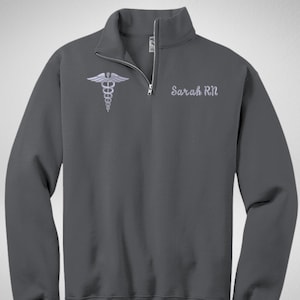 May include: A dark gray 1/4 zip sweatshirt with a white embroidered medical symbol and the text "Sarah RN" on the front.