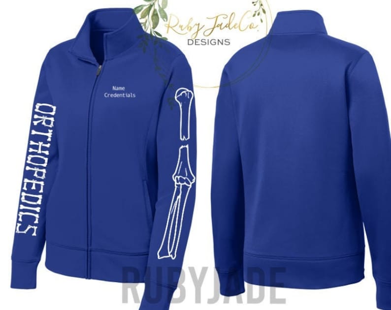 May include: A royal blue zip-up jacket with the word "ORTHOPEDICS" in white block letters down the left sleeve. The right sleeve features a white skeletal arm graphic. The jacket has a mock neck and a zipper closure. The text "Name Credentials" is above the zipper.