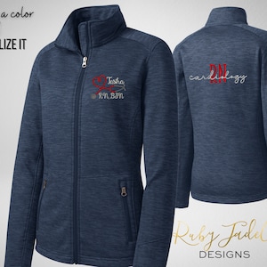 May include: A navy blue fleece jacket with a red heart and stethoscope design on the left chest. The text "Tasha RN, BSN" is embroidered below the design. The back of the jacket has the text "RN Cardiology" embroidered in red.
