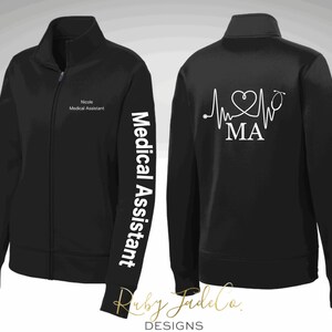 May include: Black zip-up jacket with white text on the sleeve that says "Medical Assistant" and white text on the back that says "MA" with a heart and stethoscope graphic.