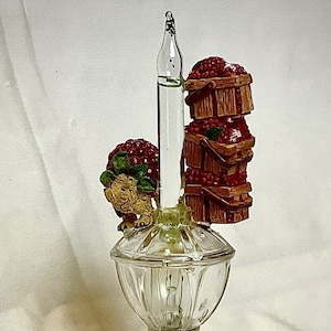 May include: A clear glass night light with a ceramic squirrel figurine and a stack of three red berry filled baskets. The night light has a blue base with an on/off switch.