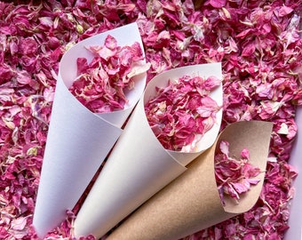 May include: Three paper cones filled with pink flower petals. The cones are made of white and brown paper. The petals are scattered around the cones.
