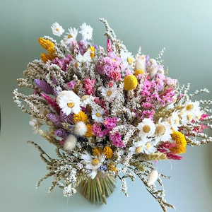 Può includere: Un bouquet di fiori secchi con fiori bianchi, gialli, rosa e viola. Il bouquet è legato con spago e ha un aspetto rustico e naturale.