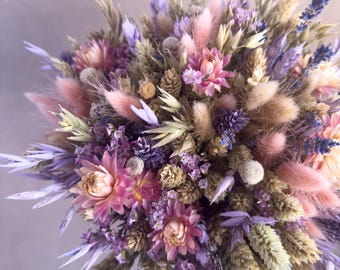 May include: A dried flower bouquet with a mix of purple, pink, and beige flowers and grasses. The bouquet is arranged in a circular shape and features a variety of textures.