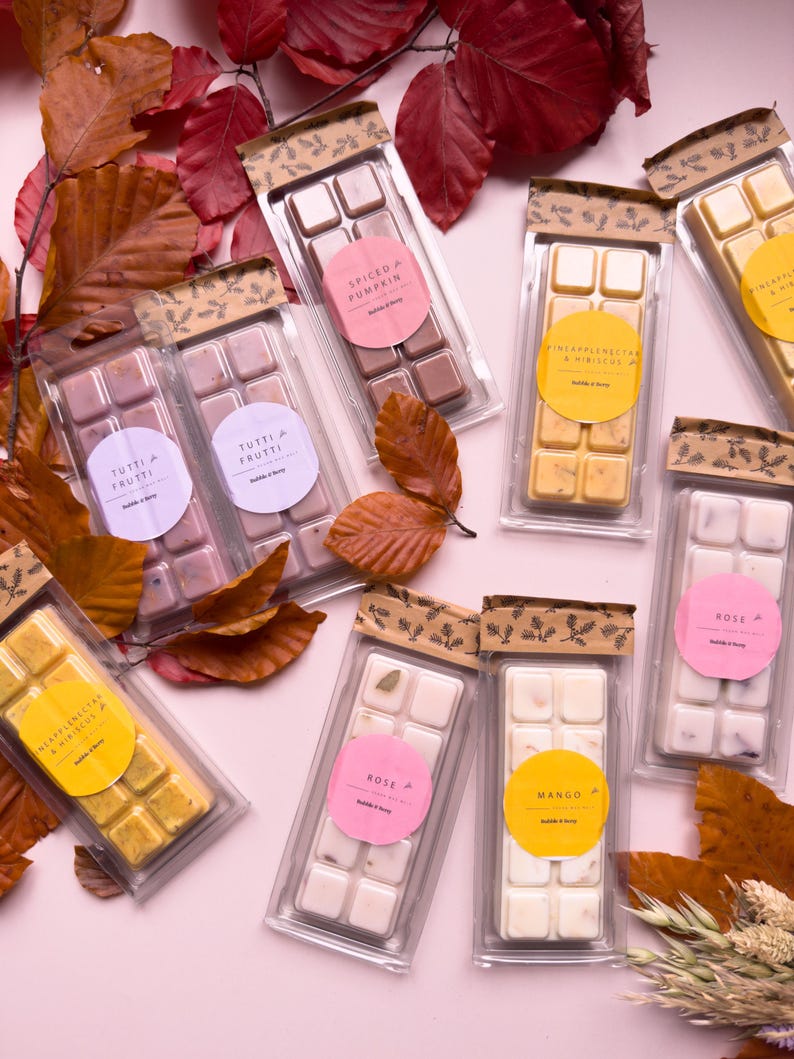 Puede incluir: Una selecci&oacute;n de barras de cera perfumada en envases transparentes, cada una con una etiqueta de aroma diferente, incluyendo "Spiced Pumpkin", "Tutti Frutti", "Pineapple Nectar & Hibiscus", "Rose" y "Mango". El fondo presenta hojas de oto&ntilde;o.