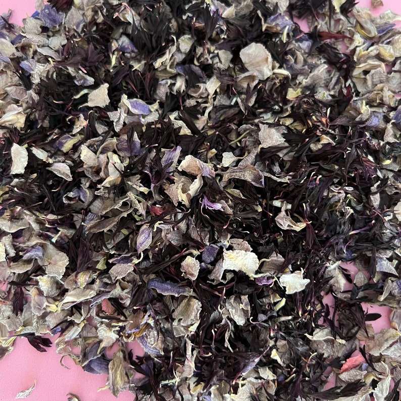 Puede incluir: Un mont&oacute;n de p&eacute;talos de flores secas en tonos de morado, blanco y marr&oacute;n. Los p&eacute;talos est&aacute;n esparcidos sobre una superficie rosa.