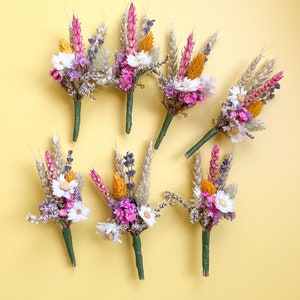 May include: Seven small bouquets of dried flowers, each with a variety of colors, including pink, purple, yellow, and white. The bouquets are arranged in a row on a yellow background.