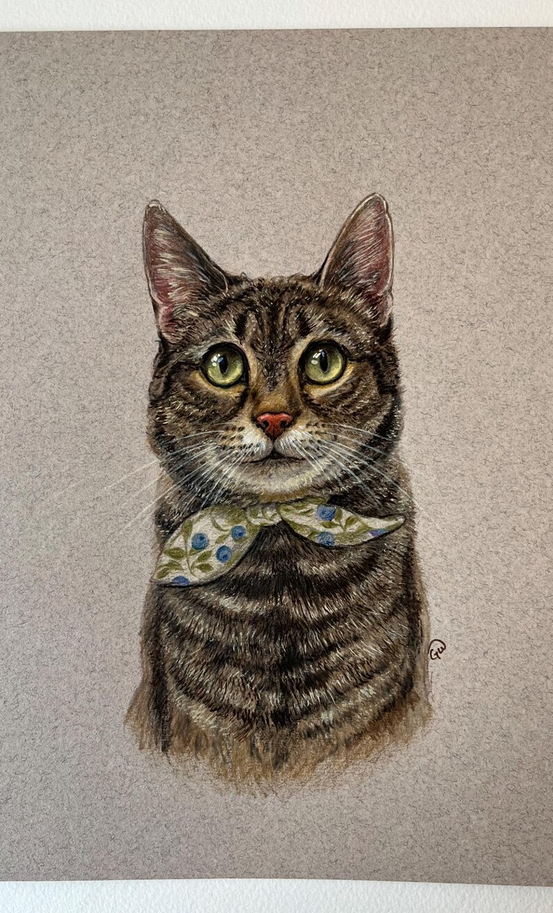 Puede incluir: Retrato detallado de un gato atigrado con ojos verdes y nariz rosa. El gato lleva una pajarita estampada con detalles florales azules. La obra de arte est&aacute; sobre un fondo gris neutro.