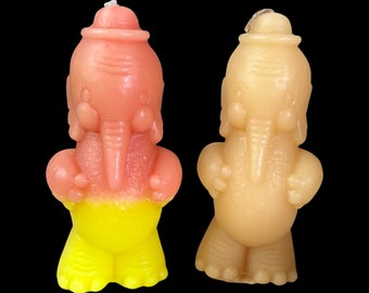 Puede incluir: Dos esculturas de velas de elefantes pintadas a mano. Una es rosa y amarilla, la otra es beige. Ambas tienen un sombrero en la cabeza y una trompa.