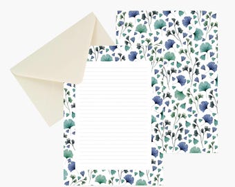 Pode incluir: Um conjunto de papelaria com um envelope de cor creme e duas folhas de papel decoradas com um padrão de folhas de ginkgo azuis e verdes. Uma folha é pautada para escrita, enquanto a outra exibe o design botânico completo das folhas.