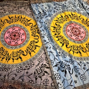 May include: Two decorative textile pieces with a circular design featuring elephants, floral patterns, and geometric borders. The central design is a yellow circle with a pink center, surrounded by black elephant silhouettes.