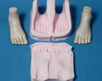 May include: A three-piece silicone mould for making baby feet. The mould is pink and has a detailed impression of two baby feet. The mould is shown with two finished baby feet made from the mould.