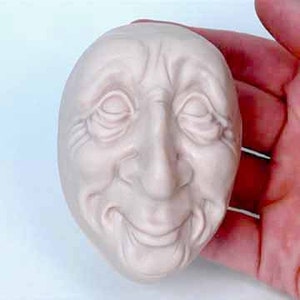 May include: A ceramic sculpture of a face with a smiling expression. The face is light brown and has a textured surface.