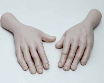 May include: Two realistic-looking, pale-toned, human hands with fingernails, lying flat on a white surface. The hands are positioned with palms facing up and fingers slightly spread apart.