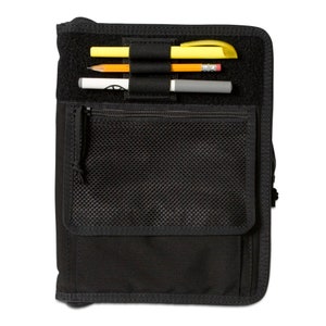 May include: A black zippered notebook with a mesh pocket and elastic pen holders. The notebook has a black zipper and a black mesh pocket. There are three pens in the elastic pen holders.