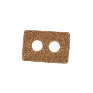 May include: A rectangular, brown felt patch with two white, circular holes. The patch has a stitched border and is set against a white background. The felt has a slightly textured appearance.