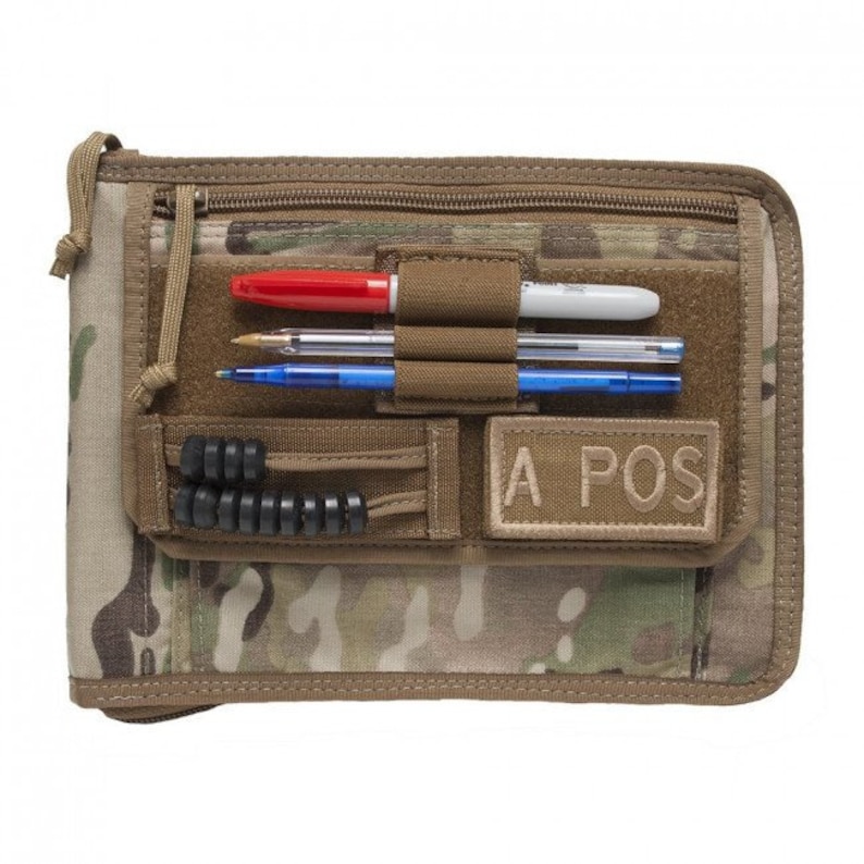 May include: A brown and tan camouflage notebook with a zipper closure. The notebook has a black elastic band, a black pen holder, and a tan patch that says "A POS".