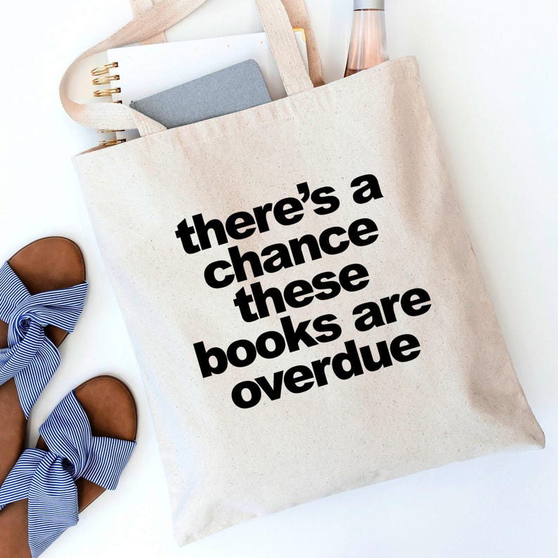 A beige tote bag with the text "there's a chance these books are overdue" printed on it, along with a pair of blue and white striped sandals.