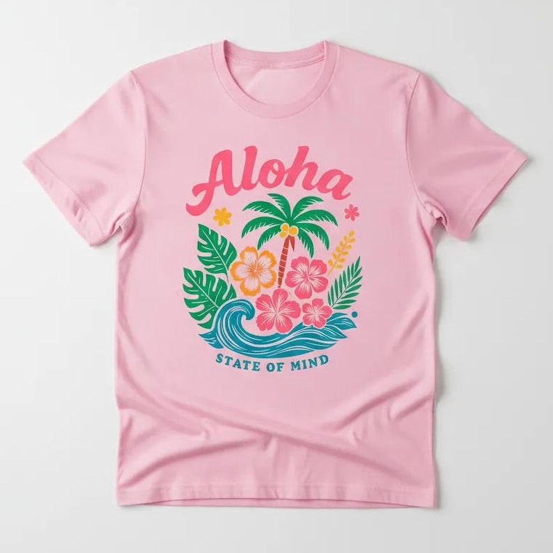 A pink t-shirt with a graphic design featuring a palm tree, flowers, and a wave, along with the text "Aloha State of Mind".
