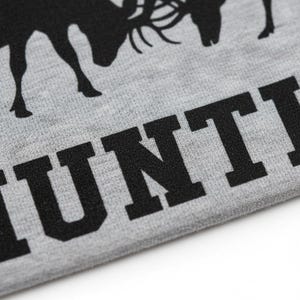 A close-up view of a grey fabric with a black silhouette of a deer and the word "HUNT" printed on it.