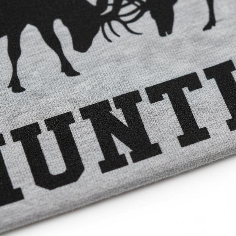 A close-up view of a grey fabric with a black silhouette of a deer and the word "HUNT" printed on it.
