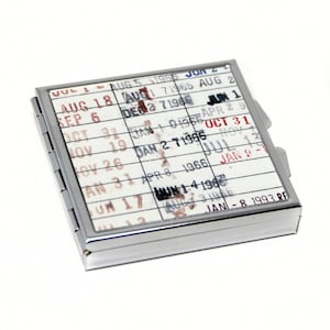 A metal coin or card holder with a calendar-like design on its surface, featuring dates and events printed on it.