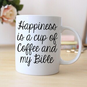 A white ceramic mug with the text "Happiness is a cup of coffee and my Bible" printed on it.
