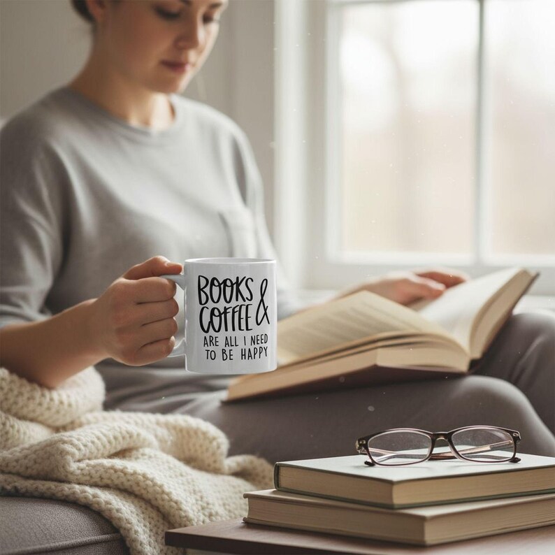 A person is sitting on a couch, holding a mug with the text "Books & Coffee are all I need to be happy" while reading a book.