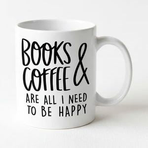 A white ceramic mug with black text that reads "BOOKS & COFFEE ARE ALL I NEED TO BE HAPPY".