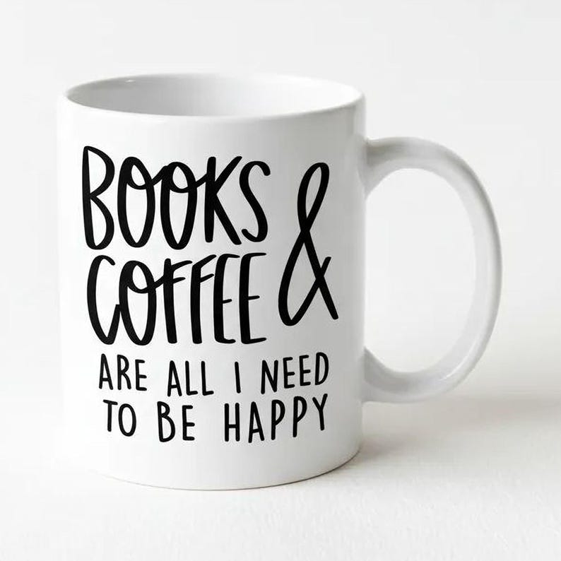 A white ceramic mug with black text that reads "BOOKS & COFFEE ARE ALL I NEED TO BE HAPPY".