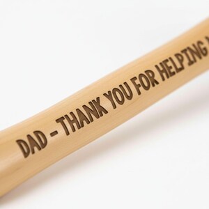 A wooden stick with the words "DAD - THANK YOU FOR HELPING" engraved on it.